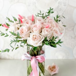 Bouquet of pale pink roses in a glass vase with a pink ribbon