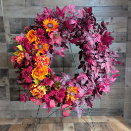 Circular wreath with orange and magenta flowers on a metal stand