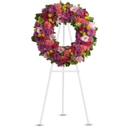 Bright pink and purple standing floral wreath on a white metal easel
