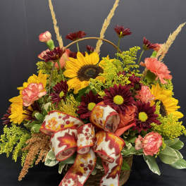 Basket arrangement with sunflowers, burgundy daisies, pink carnations, and a floral ribbon