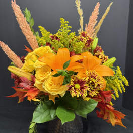 Orange lilies and yellow roses in a dark vase with autumn foliage
