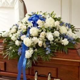 White floral casket spray with blue ribbon on a wooden casket
