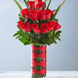Tall bouquet of red roses in a clear glass vase with red ribbon bows