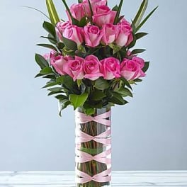 Pink roses arranged in a tall glass vase with pink ribbon