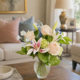 Bouquet of pale roses, lilies, and blue flowers in a glass vase