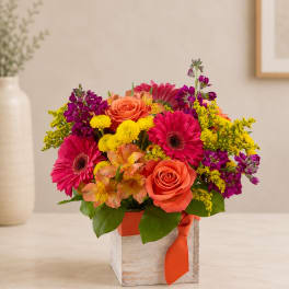 Bright mixed bouquet in a square wooden box with an orange ribbon