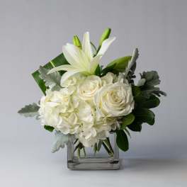 White lilies and roses arranged in a clear square vase