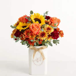 Bouquet of sunflowers, roses, and mums in a white vase with a ribbon
