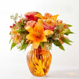 Orange and pink mixed bouquet in an amber glass vase