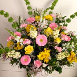 Mixed bouquet of pink and yellow flowers in a white basket vase