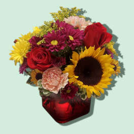 Mixed bouquet of red roses, sunflowers, and pink carnations in a red vase