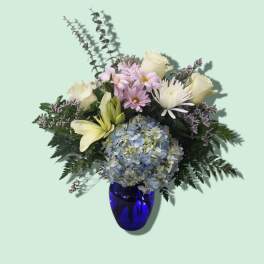 Mixed bouquet of hydrangea, roses, lilies, and daisies in a blue vase