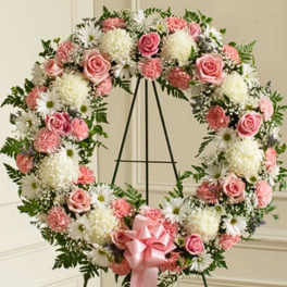 Heart-shaped wreath of pink and white flowers on a black stand with a pink bow