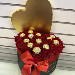 Heart-shaped box of red roses topped with gold-wrapped chocolates and a red ribbon