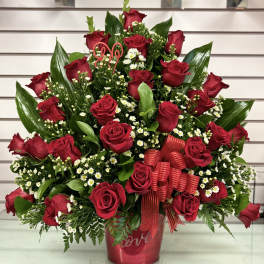 Red roses arranged in a red vase with small white filler flowers and ribbon