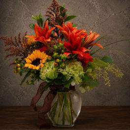 Bouquet of orange lilies, a sunflower, and green hydrangeas in a glass vase