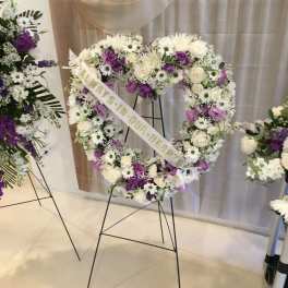 Heart-shaped floral wreath on a stand with white and purple flowers