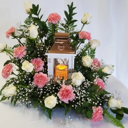 White roses and pink carnations arranged around a lantern centerpiece