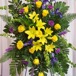 Large standing floral spray with yellow roses, lilies, and purple flowers