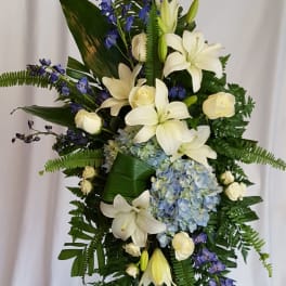 Tall floral standing spray with white lilies, roses, blue hydrangea, and purple delphinium