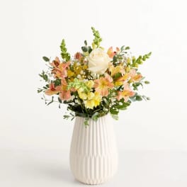 Mixed bouquet of peach and yellow flowers in a white vase