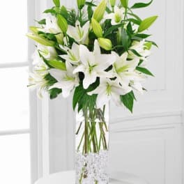 Tall arrangement of white lilies and buds in a clear glass vase with glass gems