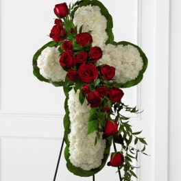 Cross-shaped floral tribute with red roses and white flowers on an easel