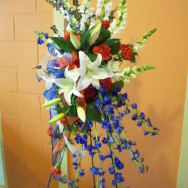 Tall standing floral spray with white lilies, red carnations, and blue flowers