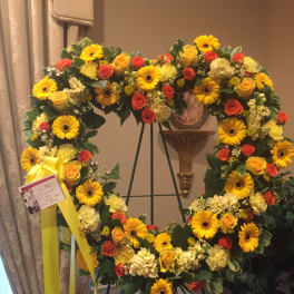 Large yellow and orange floral wreath on an easel with a ribbon and card