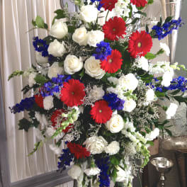 Large standing floral spray with red gerberas, white roses, and blue flowers
