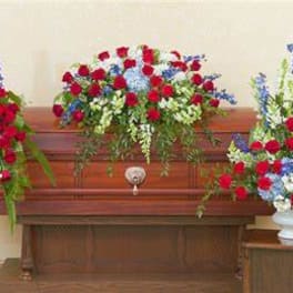 Three red, white, and blue floral sprays arranged around a wooden casket