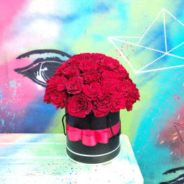 Red roses arranged in a black round box with a pink ribbon