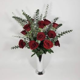 Red roses arranged in a tall white vase with eucalyptus