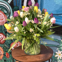 Mixed tulips and small white daisies in a clear glass vase
