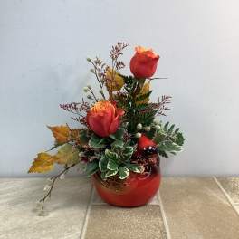 Two red-orange roses in a red ceramic vase with autumn leaves
