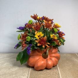 Fall flower arrangement in a pumpkin-shaped container with orange, yellow, and purple blooms