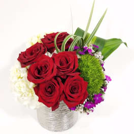 Red roses arranged in a silver vase with white and purple accents