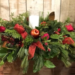Holiday centerpiece with a white candle, red roses, and evergreen foliage