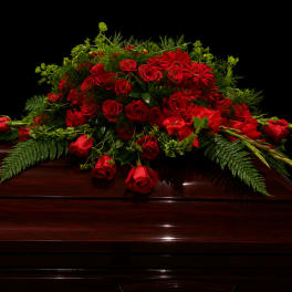 Red rose casket spray with greenery on a dark wood casket