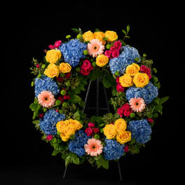 Heart-shaped floral wreath with blue hydrangeas, yellow roses, and pink gerbera daisies