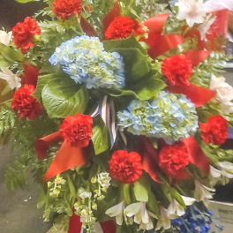 Large standing floral spray with red carnations, blue hydrangeas, and white lilies