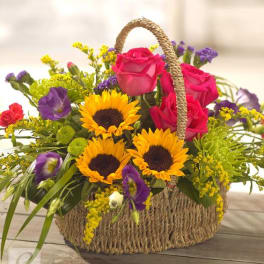 Basket arrangement with pink roses, sunflowers, and purple blooms