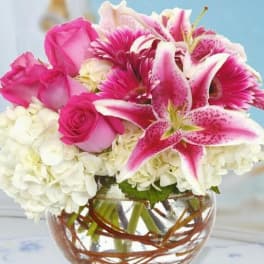 Pink roses and lilies arranged with white hydrangeas in a glass bowl vase