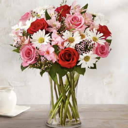 Bouquet of pink and red roses with white daisies in a clear glass vase
