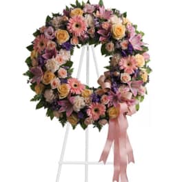 Pastel floral wreath on a white stand with a pink ribbon