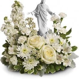 White floral arrangement with roses, carnations, and a central white robed figurine.