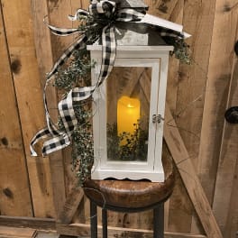 White lantern with a glowing candle, greenery, and black-and-white ribbon