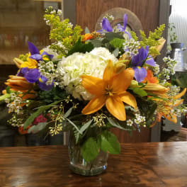 Mixed bouquet in a clear glass vase with orange lilies and purple irises