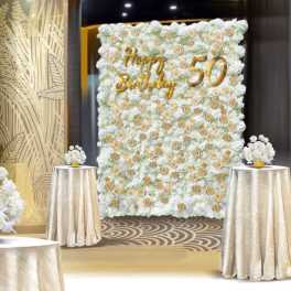 White floral wall with gold "Happy Birthday 50" lettering and matching table arrangements