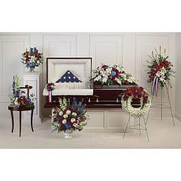 Funeral casket surrounded by red, white, and blue floral sprays